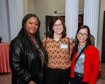 Three people pose for a photo at a conference dinner with large white columns in the background.