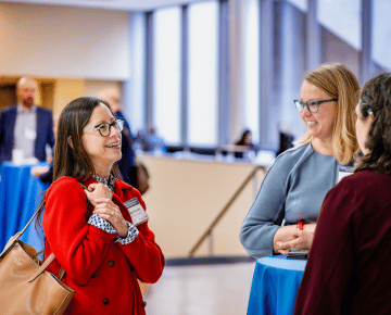 Three individuals conversing at a networking event, with two women in the foreground smiling and engaged in conversation and engaged in-depth discussion.
